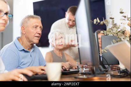Focused older gentleman using computer at internet cafe Stock Photo