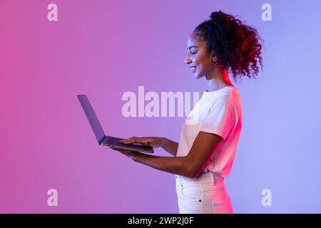 Smiling black woman using laptop with neon light background Stock Photo