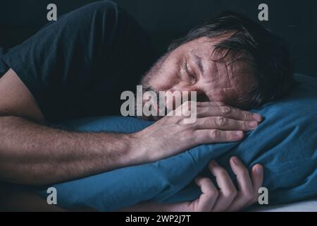 Tired asleep adult male in a bed on blue pillow, selective focus Stock Photo