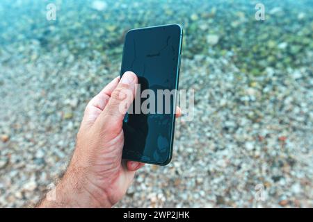 Man holding wet waterproof mobile phone found in sea water, selective focus Stock Photo