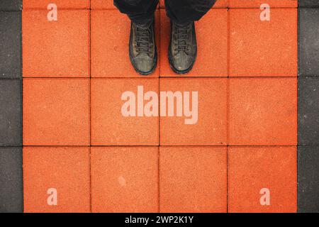 Man standing on the square shaped concrete pavement slabs, top view of dirty boots on orange sidewalk with copy space Stock Photo