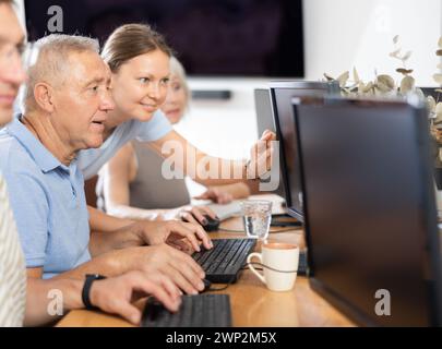 Young female mentor explaining something to elderly man during computer class Stock Photo