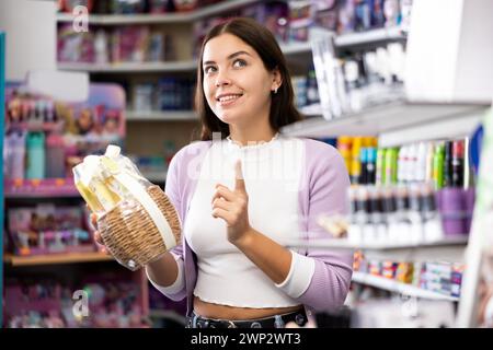 Positive young woman holding kit of haircare products in cosmetics shop Stock Photo