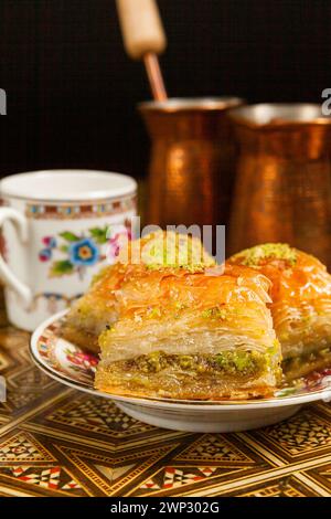 Still life with hot oriental coffee brewed in cezve. On the Arabic table is a small coffee cup and delicious honey baklava with pistachios on a saucer Stock Photo