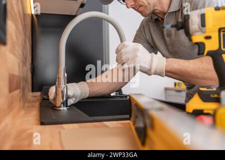 Caucasian Professional Plumber Installing Kitchen Sink and a Faucet Stock Photo