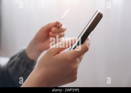 Close up of female hands holding credit card and smartphone, unknown girl paying online, using banking service, entering information, shopping, orderi Stock Photo