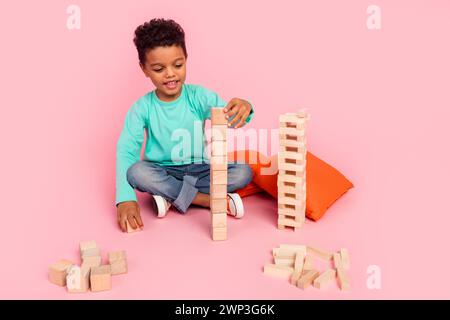 Full size photo of charming small boy play wooden cubes tower wear trendy aquamarine outfit isolated on pink color background Stock Photo