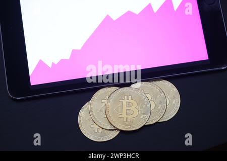 Symbolbild:  Bitcoins vor einem Tablet mit Finanzdaten - Der Bitcoin steht hoch im Kurs. Selbst Finanzdienstleister wie Paypal wollen die Kryptowährun Stock Photo