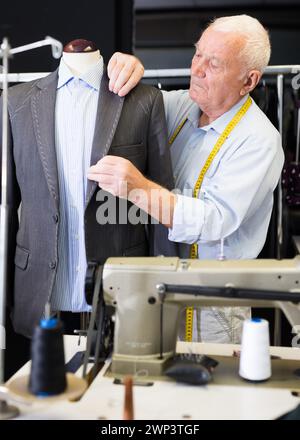 Mature tailor sews a new jacket on a mannequin in sewing studio Stock ...