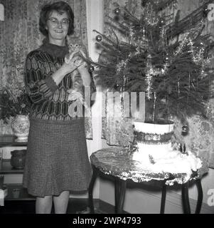 1960s, historical, a woman standing by a small xmas tree on a table, holding in her hands a kitten, England, UK. Stock Photo