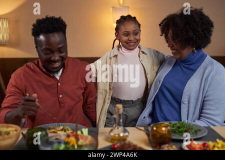 Waist up portrait of cute african American girl with parents at dinner table all family smiling happily Stock Photo