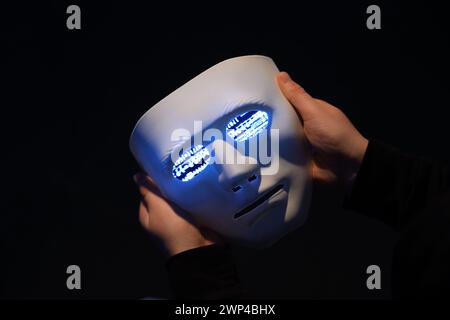 Hacker holding mask with programming code on dark background, closeup Stock Photo