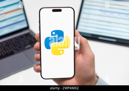 PRAGUE, CZECH REPUBLIC - JANUARY 21 2024: Python logo on the screen of smartphone in mans hand on the workplace background.  Stock Photo