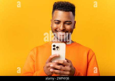 Happy Indian man in casual clothes using smartphone isolated on yellow, guy chatting online, using new mobile app, texting with girlfriend Stock Photo