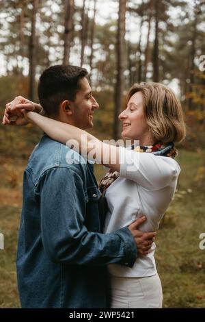 Happy man and a woman are embracing each other in the forest in autumn, smiling happily with their arms wrapped around each other Stock Photo