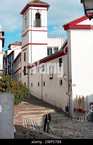 The Albaicín neighbourhood, Granada, Spain. A man sweeps the cobbled area in front of the Iglesia de San Gregorio with its minaret-like church tower. Stock Photo