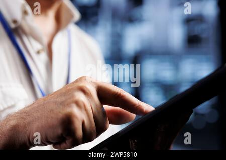 Qualified electrician inspects server rows in computer network security data center, ensuring optimal performance. Certified wireman monitoring energy consumption across infrastructure parts, close up Stock Photo