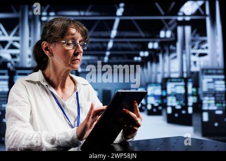 Old computer scientist using tablet to assess server cybersecurity problems arising due to unsecured network connections. Adept worker ensuring high tech location is impenetrable by ddos attacks Stock Photo