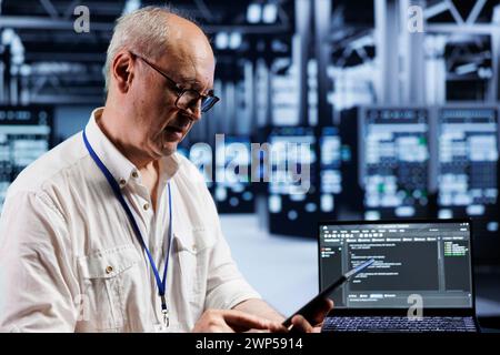 Aged precise engineer coding in technologically advanced data center using javascript language. Expert updating software on server racks on laptop terminal, ensuring errorless performance and security Stock Photo