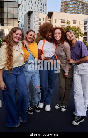 Multiracial group of smiling young women standing together embraced outdoors in an urban area. Stock Photo