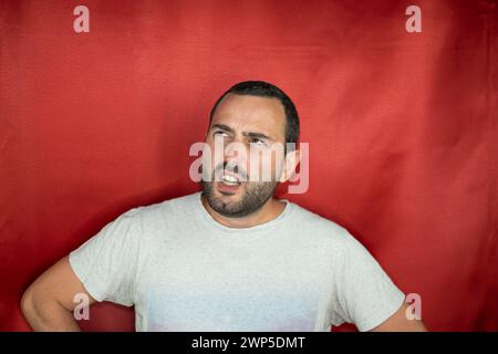 Hispanic young adult man thoughtful looking up indecisive and confused with idea Stock Photo