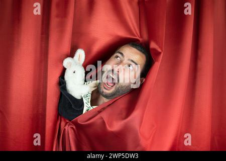 Funny young adult man magician with Hurt face playing with evil rabbit out hat Stock Photo
