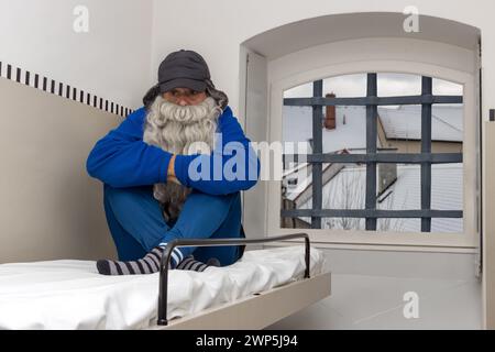 A bearded man sits on a bunk in a cold prison cell Stock Photo