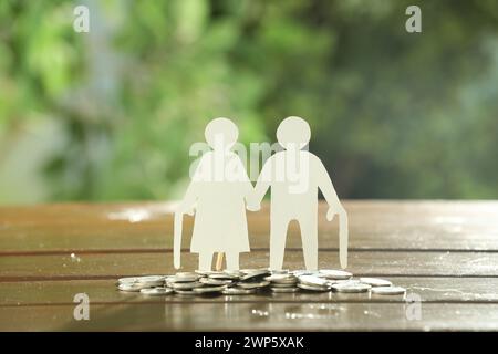 Pension savings. Figure of senior couple and coins on wooden table outdoors Stock Photo