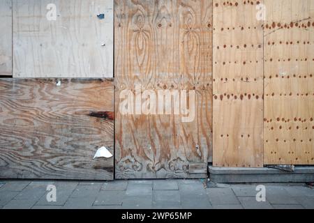 A detailed view of a sidewalk bordered by a diverse patchwork of plywood sheets, featuring an array of textures and patterns due to different wood. Stock Photo