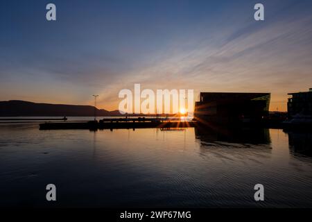 Sun rising behind mountains near Reykjavik casts rays over calm water of the Old Harbour Stock Photo