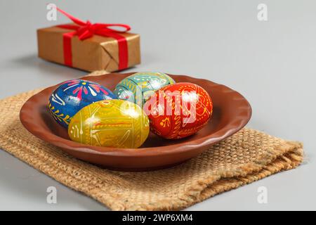 Clay plate with painted Easter eggs on the sackcloth bag, a gift box on the gray background. Stock Photo