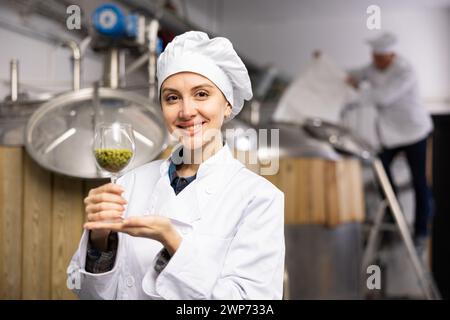 Successful female brewmaster showing hop pellets in glass Stock Photo