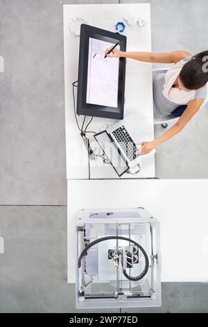 3D, printing and designer in office, working on monitor and above desk with planning on tech for rendering. Prototype, printer and aerial view of Stock Photo