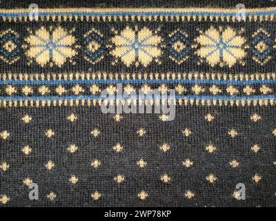 A fragment of an ornament on a knitted polyester or woolen sweater. Flowers. Winter motives. Blue threads for hand knitting. White thread knitted Stock Photo