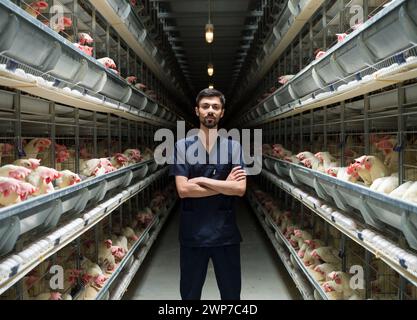 Portrait of young veterinarian on egg farm.  Man in uniform working on chicken farm and chickens in background Stock Photo