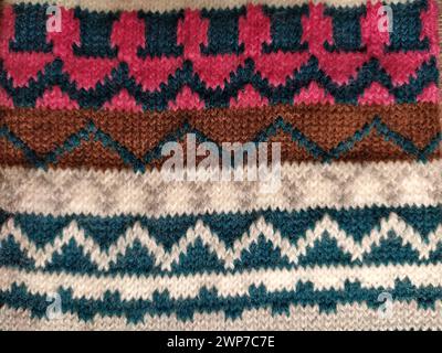 A fragment of an ornament on a knitted polyester or woolen sweater. Winter motives. Rhombuses, broken lines, waves. Knitted pattern from white, pink, Stock Photo