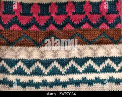 A fragment of an ornament on a knitted polyester or woolen sweater. Winter motives. Rhombuses, broken lines, waves. Knitted pattern from white, pink, Stock Photo