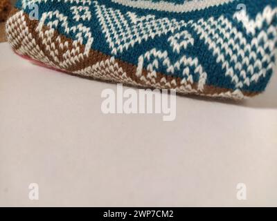 A fragment of an ornament on a knitted polyester or woolen sweater. Winter motives. Rhombuses, broken lines, waves. Knitted pattern from white, pink, Stock Photo