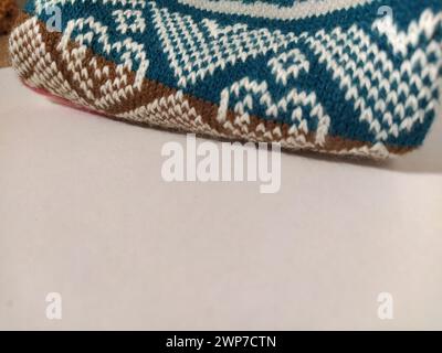 A fragment of an ornament on a knitted polyester or woolen sweater. Winter motives. Rhombuses, broken lines, waves. Knitted pattern from white, pink, Stock Photo
