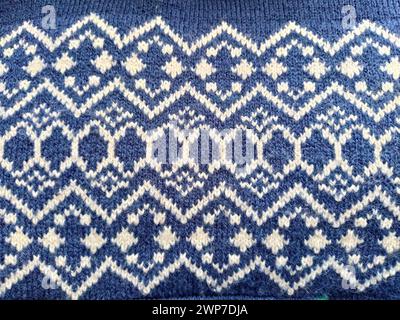 A fragment of an ornament on a knitted polyester or woolen sweater. Winter motives. Blue threads for hand knitting. Knitted pattern from a white threa Stock Photo