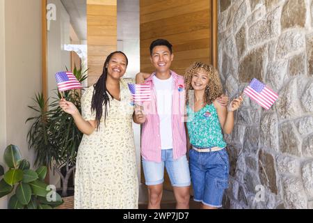 Diverse friends hold American flags at a home entrance Stock Photo
