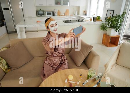 Cheerful beauty blogger with clay mask taking selfie Stock Photo