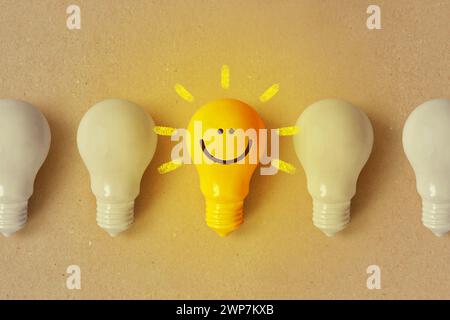 Glowing yellow light bulb with smile and white light bulb turned off - Positive thinking and standing out from crowd concept Stock Photo