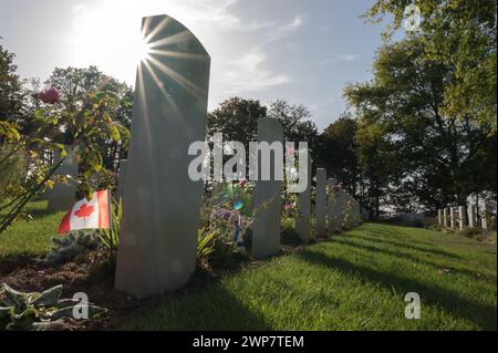 Detail of a Canadian flag on a headstone at the Canadian War Cemetery. It is a backlit photograph with the star effect in the sun. Stock Photo