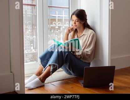 Concentrated young woman sitting on the floor with notebook in hand Stock Photo