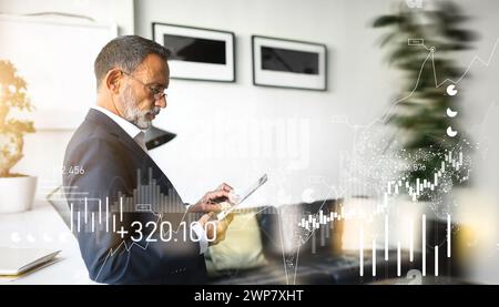 Mature businessman in a suit attentively examines his tablet, standing in a modern office Stock Photo