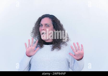 blonde, curly-haired, blue-eyed woman with a surprised gesture and raised hands Stock Photo