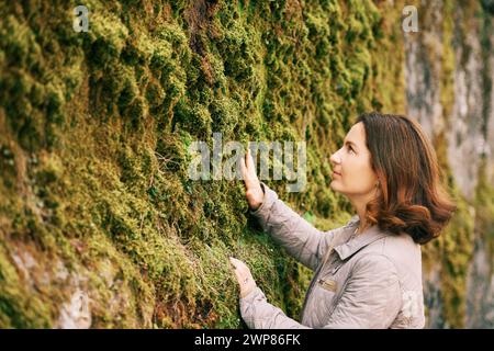Outdoor portrait of happy beautiful woman enjoying nice day outside, posing with moss wall Stock Photo