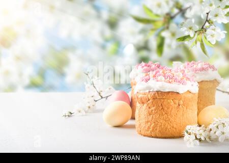 Traditional Easter cake with white swiss meringue and pink sweet decoration and colorful painted eggs on background blooming cherry or apple garden fl Stock Photo