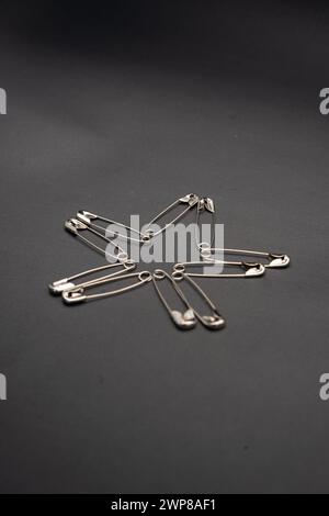 Safety pins arranged in a star shape isolated on dark black background. Stock Photo